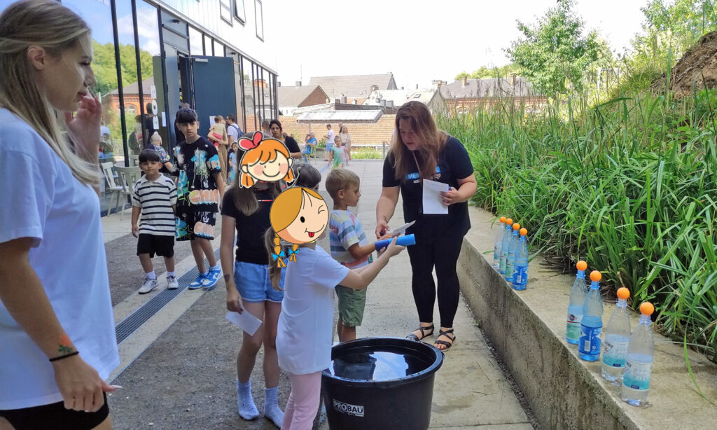 Kinder versuchen mit einer Spritze bunte Tischtennisbaelle von Flaschen herunterzuschiessen