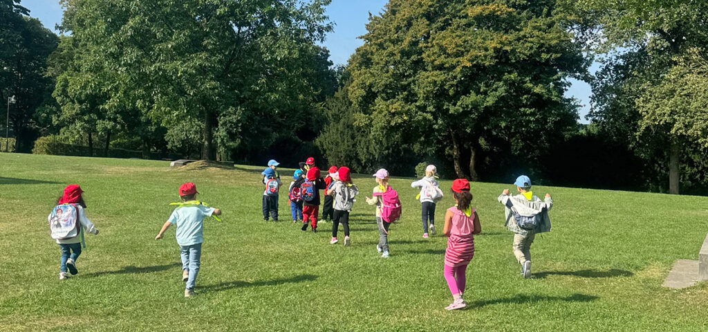 Kinder mit bunten Kappen auf dem Kopf laufen ueber eine grosse Wiese