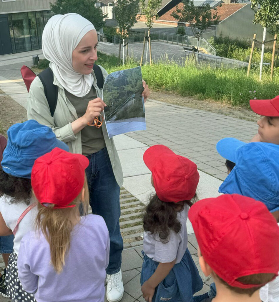 Kinder schauen in einem grossen Garten auf das Bild, das ihnen die Erzieherin zeigt