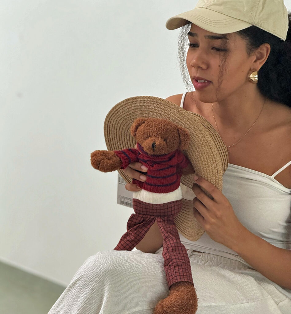 Eine Frau haelt einen Stoffteddy in den Haenden der einen grossen Hut traegt