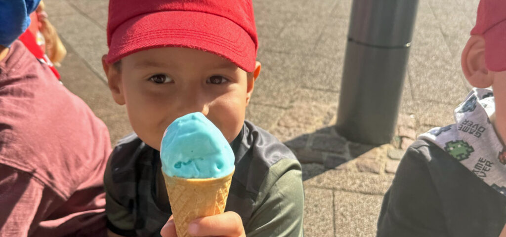 Ein Kind zeigt seine Eiswaffel mit einer Kugel blauem Eis darin