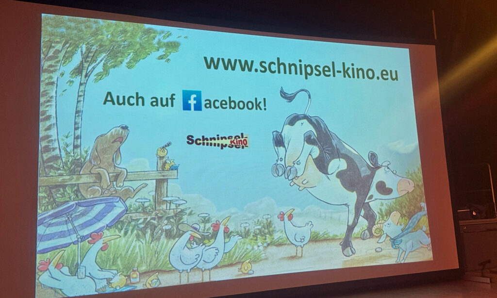 Auf einer Leinwand mit dem Schriftzug Schnipselkino sind eine Kuh, ein Hund und Huehner zu sehen