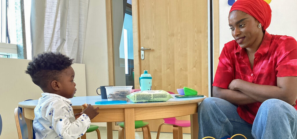 Eine Frau sitzt mit einem Kind an einem kleinen Tisch in der Kita