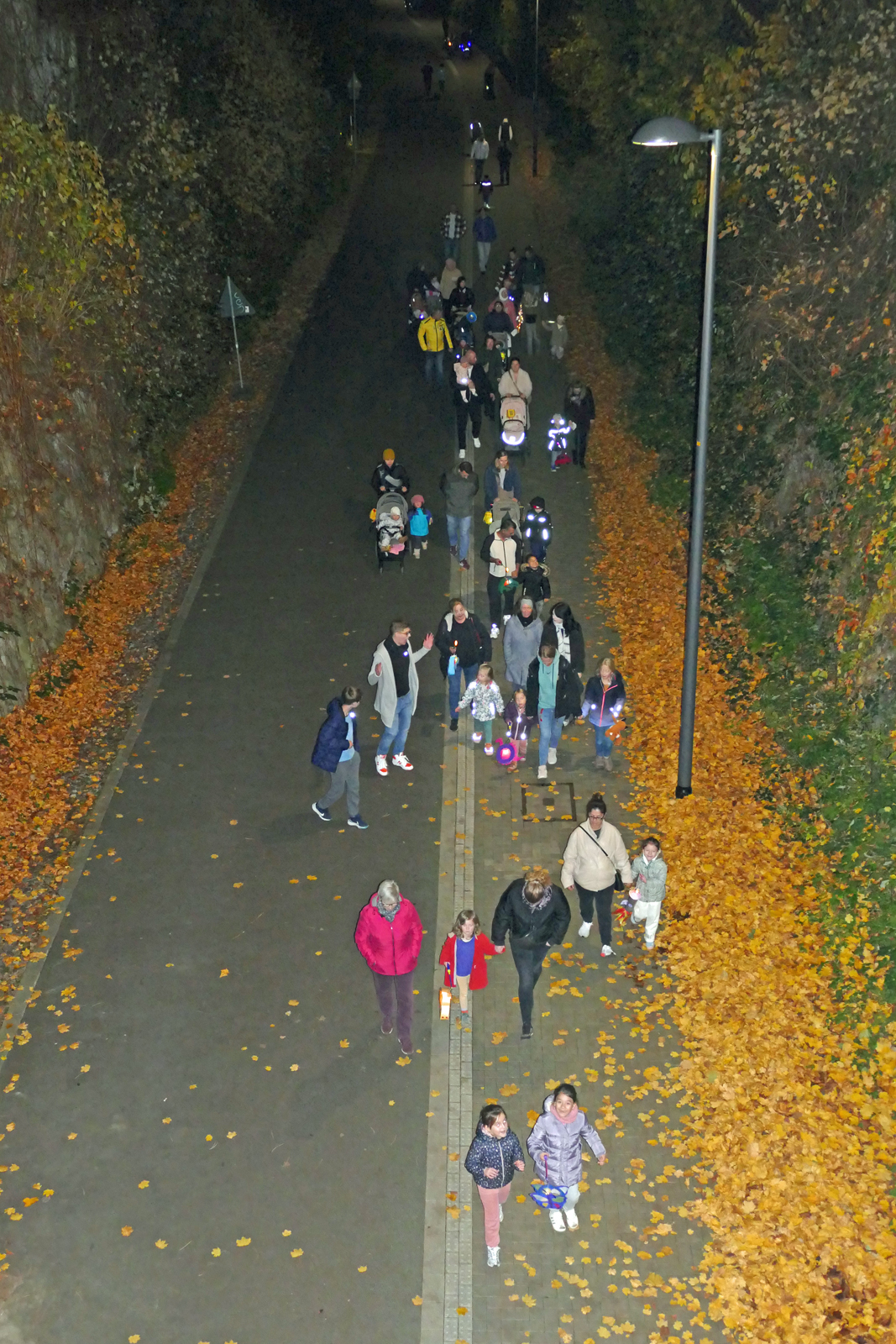 Kinder und Erwachsene gehen in der Dunkelheit mit leuchtenden Laternen ueber die Nordbahntrasse