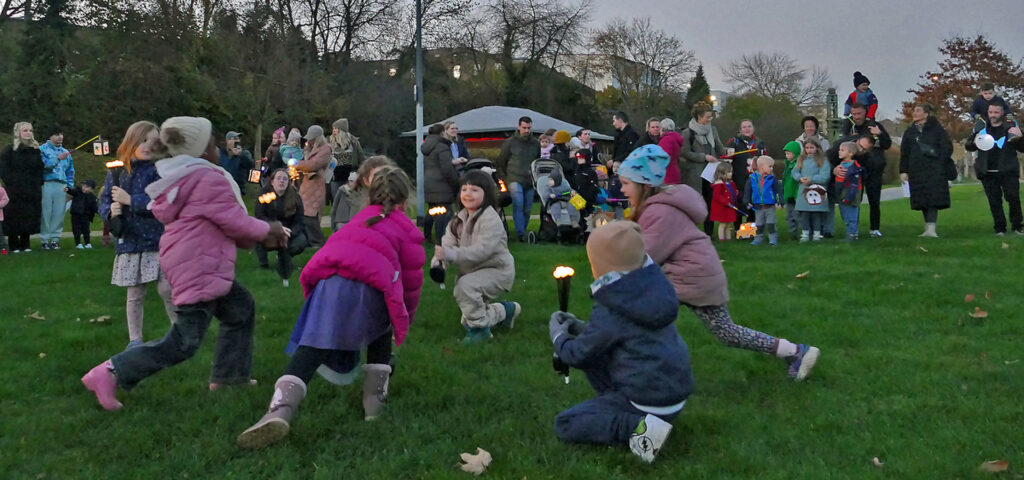 Kinder fuehren auf einer Wiese vor Zuschauern einen Tanz mit LED-Leuchten auf