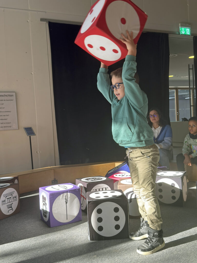 Ein Kind hebt einen grossen leichten Wuerfel hoch um ihn zu werfen