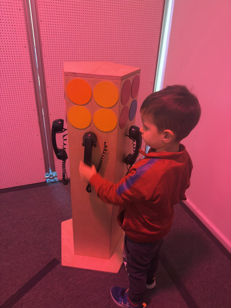 Ein Kind nimmt im Akki Museum einen schwarzen Telefonhoerer in die Hand