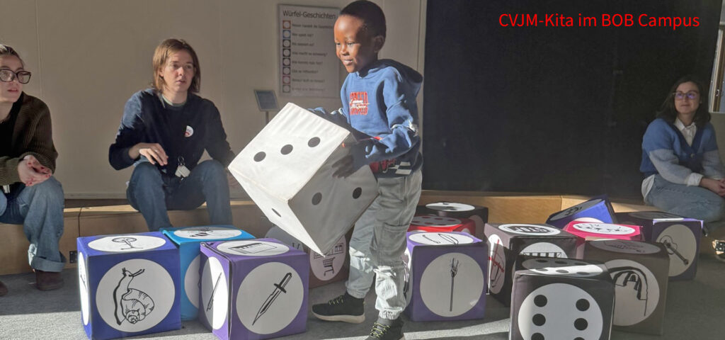 Ein Kind haelt einen grossen Zahlenwuerfel in den Haenden und laesst sich von einer Frau etwas erklaeren