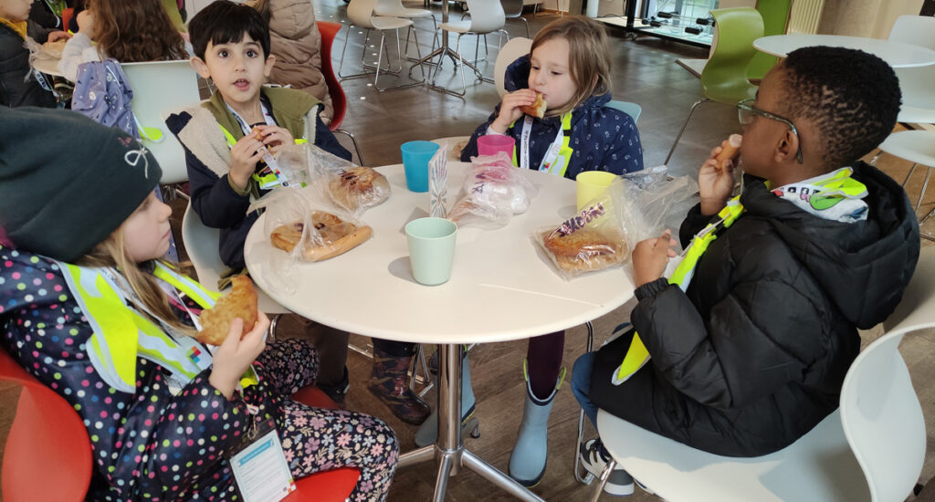 Kinder sitzen mit Jacken bekleidet an einem Tisch in einem Schnellrestaurant