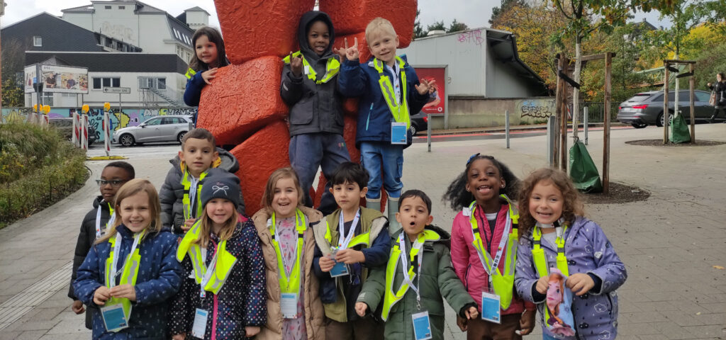 Kinder haben sich an einer roten Steinskulptur fuers Gruppenfoto aufgestellt