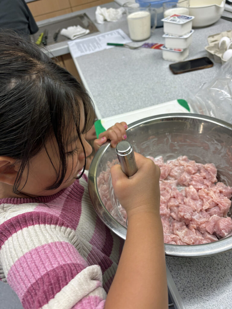 Ein Kind verruehrt in einer Schuessel Fleisch mit Speisestaerke