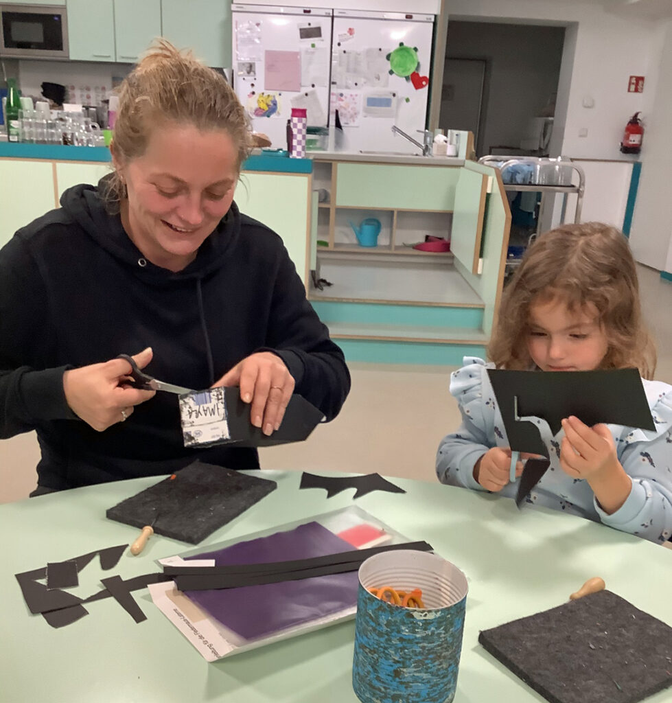 Eine Frau und ein Kind sitzen am Tisch und schneiden etwas aus schwarzer Pappe aus