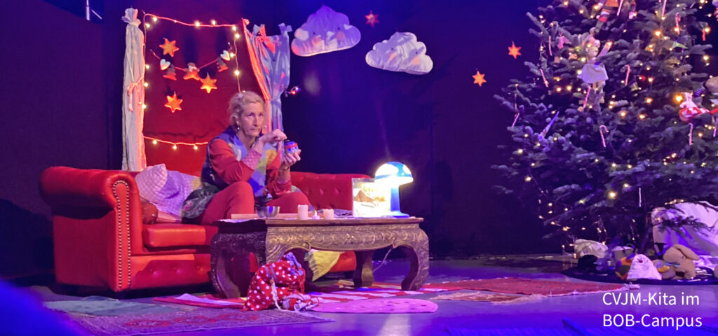 Miss Fairytaile sitzt auf einem Sofa auf der Buehne neben einem praechtig geschmueckten Weihnachtsbaum