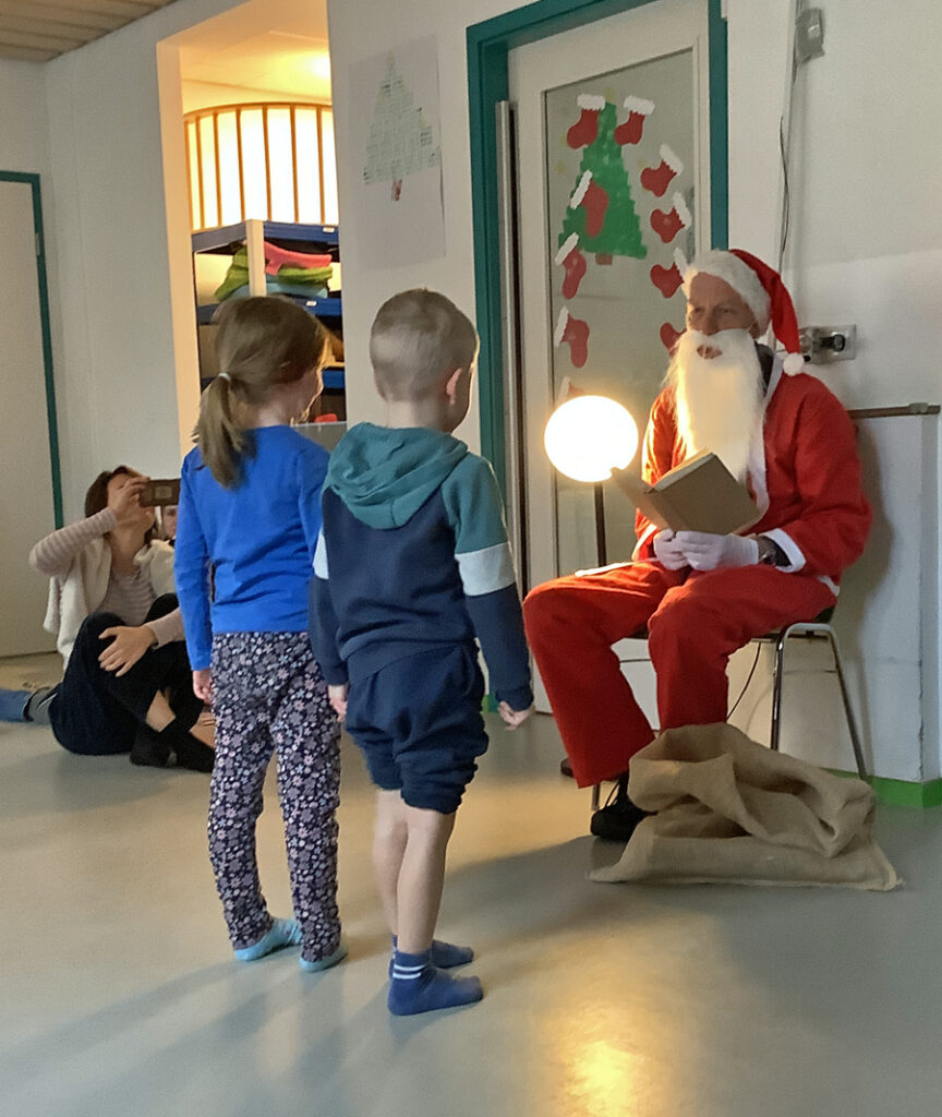 Zwei Kinder stehen vor dem Nikolaus und hoeren was er zu erzaehlen hat