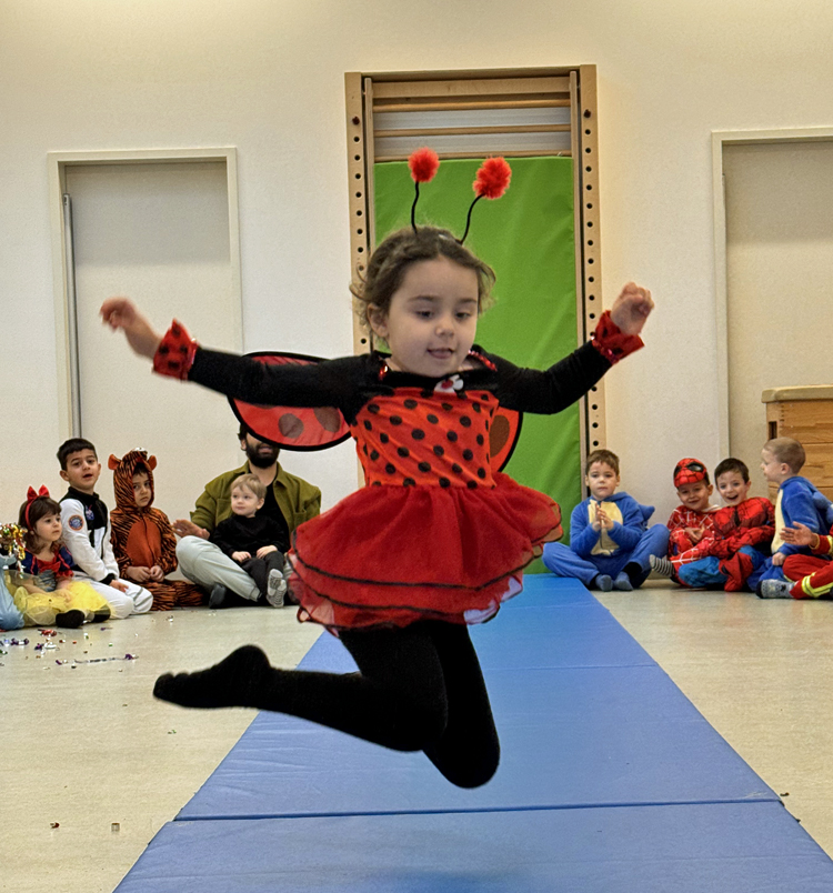 Ein Kind im Marienkaefer-Kostuem springt auf einer Turnmatte hoch in die Luft
