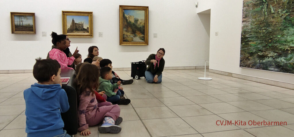 Kinder und Erwachsene sitzen im Von-der-Heydt-Museum vor einem grossen Gemaelde