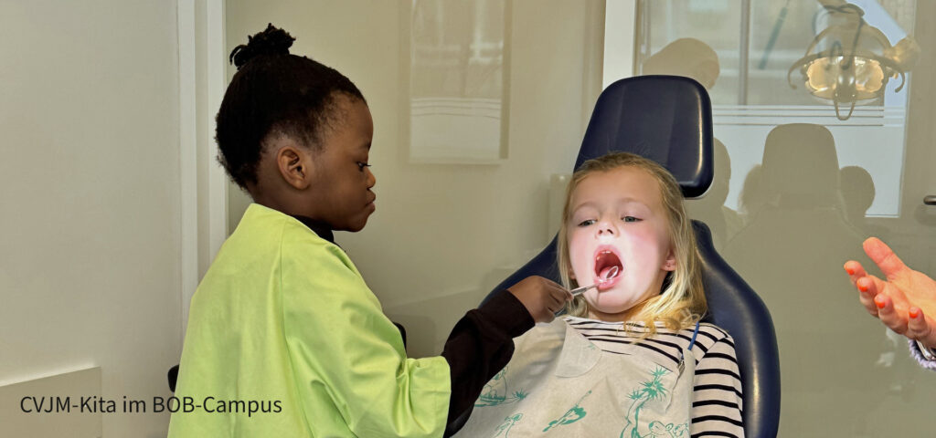 Ein Kind untersucht die Zaehne eines anderen Kindes auf dem Zahnarztstuhl