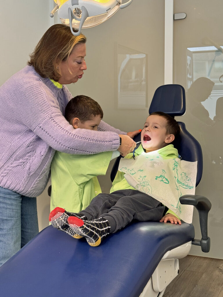 Die Mitarbeiterin des Mundhygienezentrums und ein Kind schauen in den Mund eines anderen Kindes