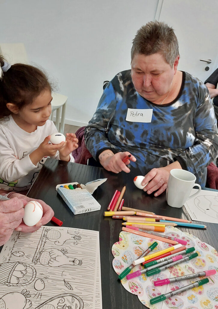 Ein Kind und eine aeltere Frau malen am Tisch Ostereier bunt