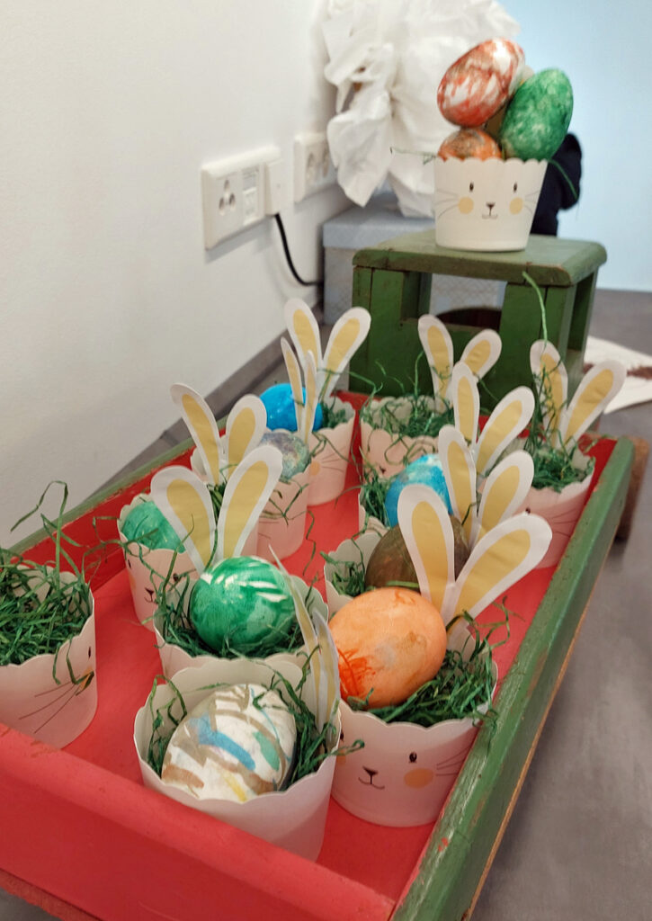 Auf einem Tablett stehen kleine Hasen-Osterkoerbchen mit bunten Eiern darin