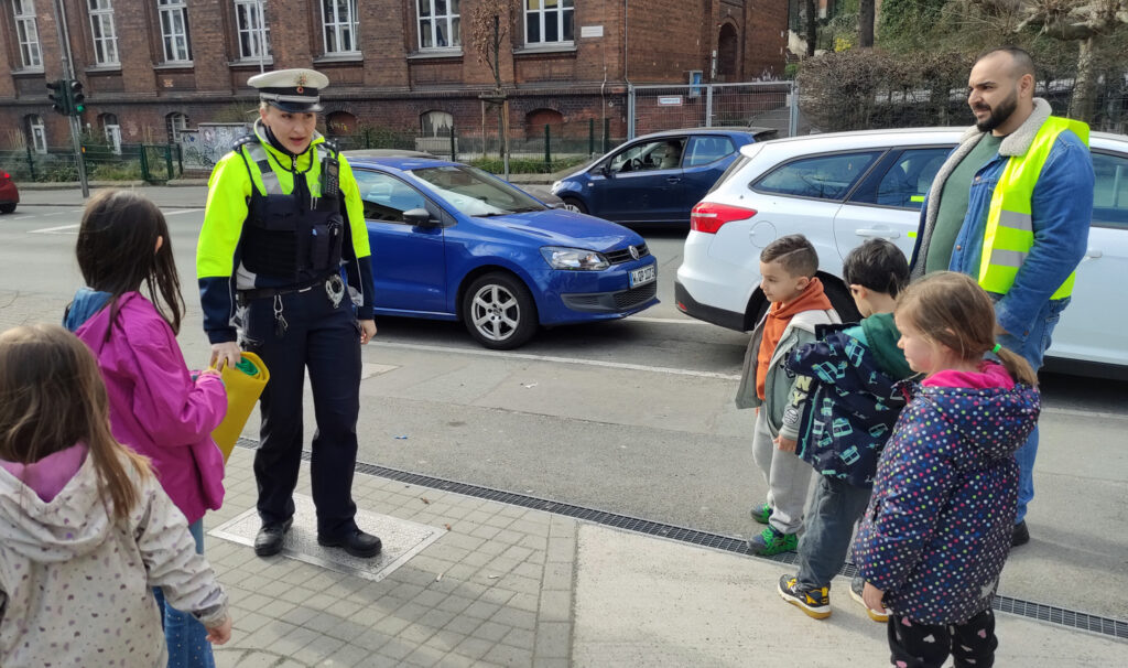 Eine Polizistin erklaert Kita-Kindern etwas draussen auf dem Gehweg