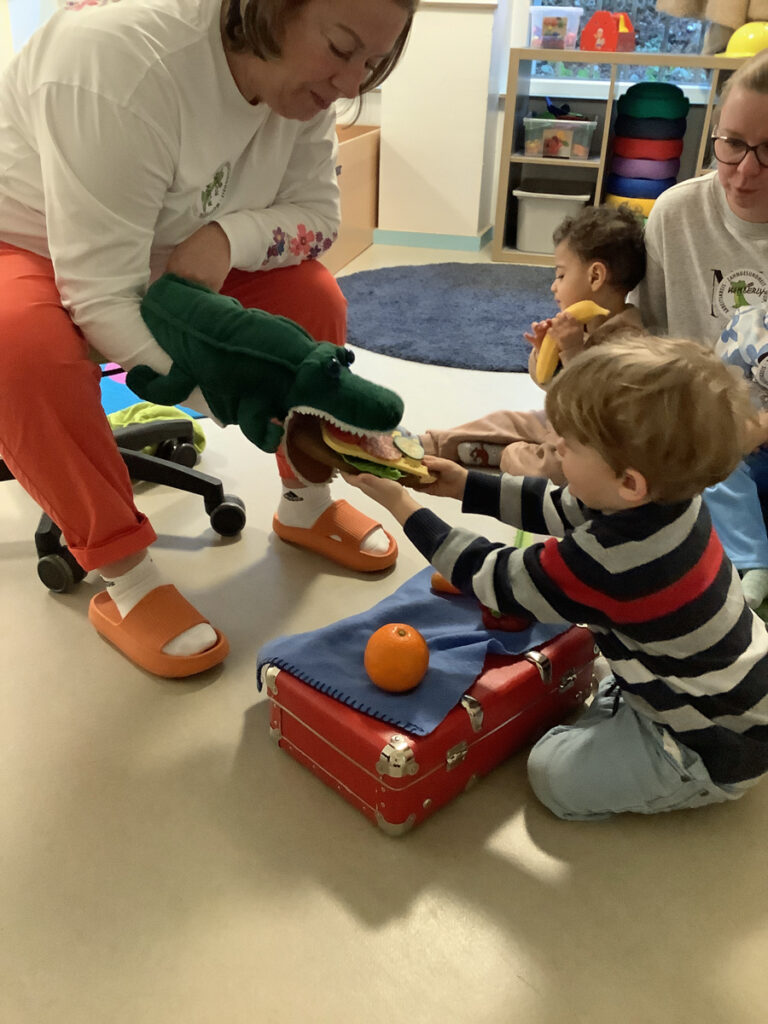 Ein Kind fuettert das gruene Zahnkrokodil Mickey mit einem Butterbrot