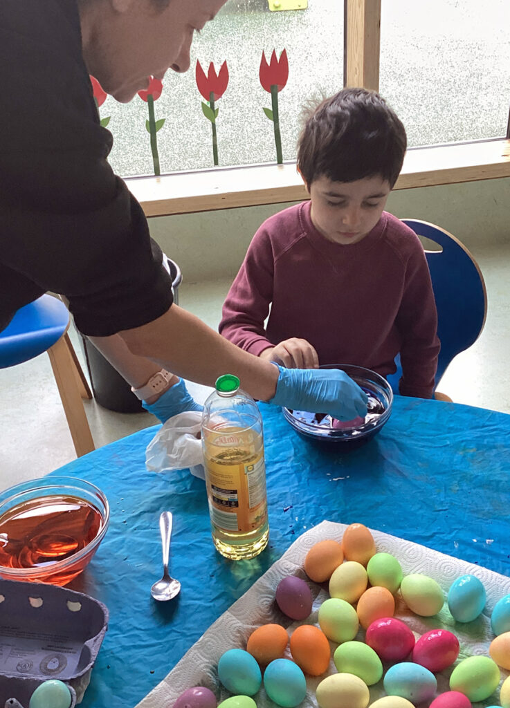 Eine Erzieherin und ein Kind faerben gemeinsam Ostereier