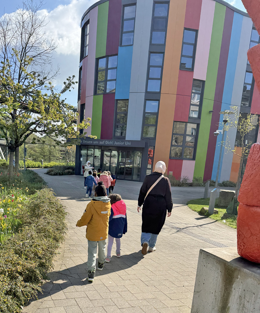 Kinder und Erzieherinnen gehen zum Eingang des bunten Gebaeudes der Junioruni Wuppertal