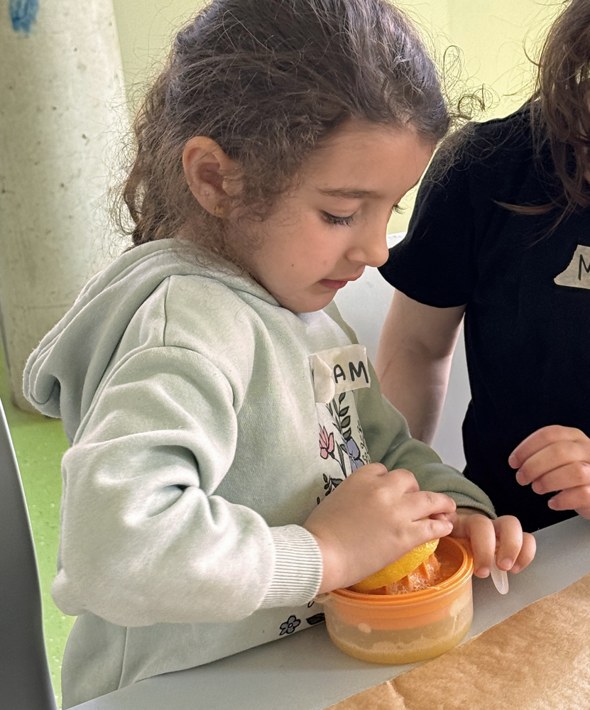 Ein Kind steht am Tisch und presst eine halbe Zitrone aus