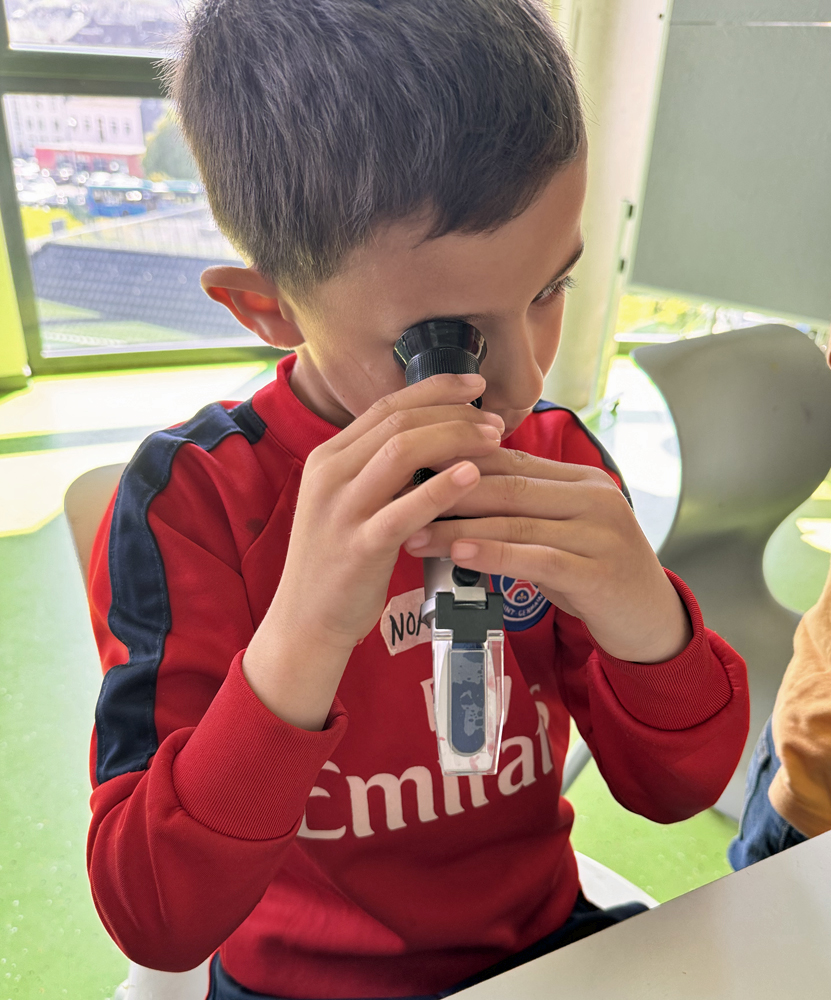 Ein Kind sitzt am Tisch in der Junioruni und schaut in ein Refraktometer