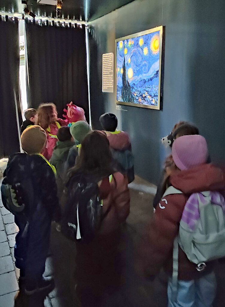 An der Wand in einem daemmrigen Raum haengt ein farbenfrohes Gemaelde und Kinder schauen es an