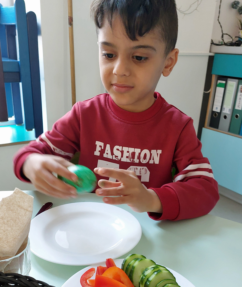 Ein Kind sitzt am Tisch beim Fruehstueck und hat sich ein farbiges Ei genommen