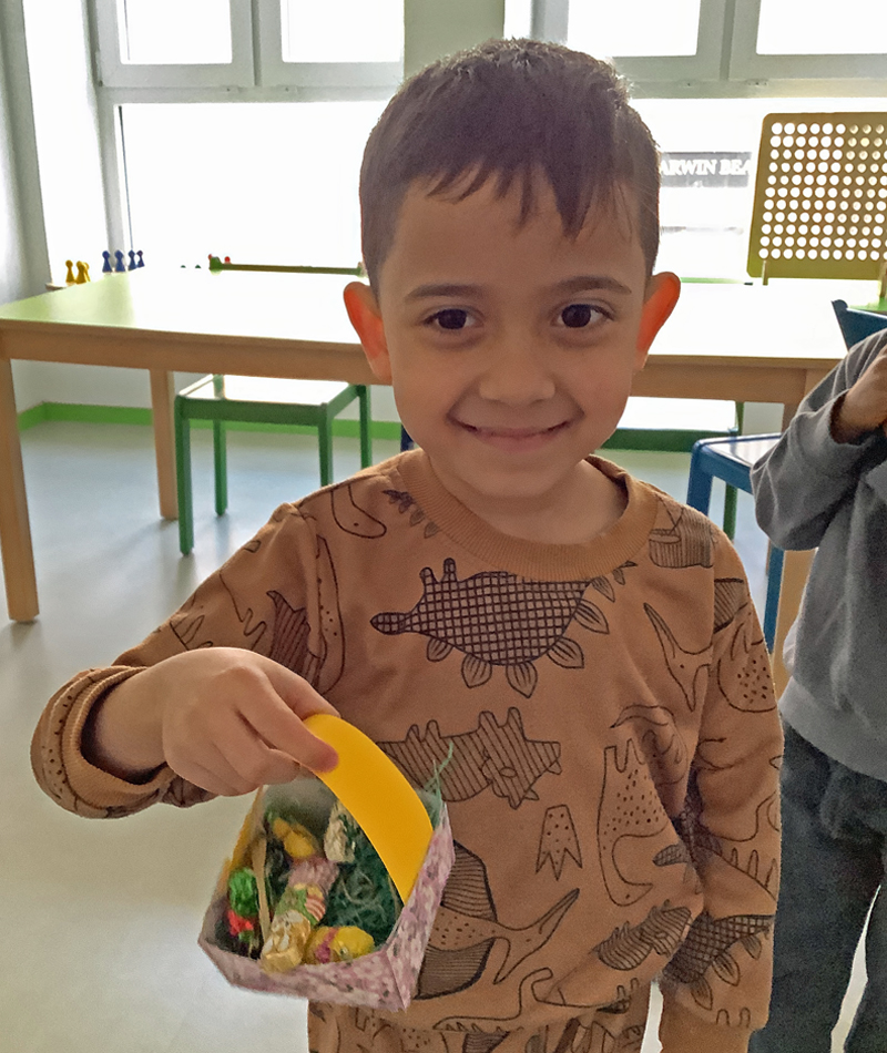 Ein Kind zeigt laechelnd sein Osterkoerbchen mit Suessem darin