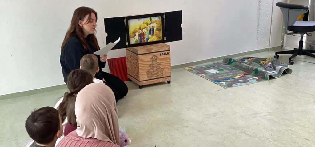 Eine Frau liest Kindern eine Geschichte vor und zeigt Bilder dazu