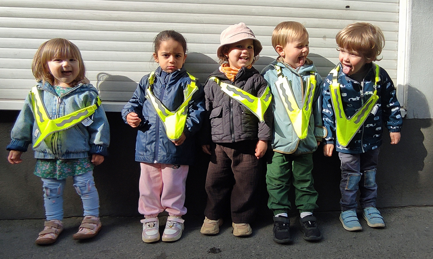 Kinder stehen draussen in der Sonne vor einem Rolladen und lachen in die Kamera