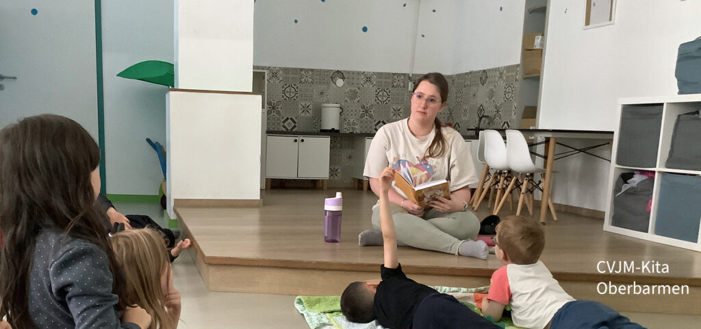 Eine Erzieherin sitzt auf dem Boden und liest Kindern ein Buch vor