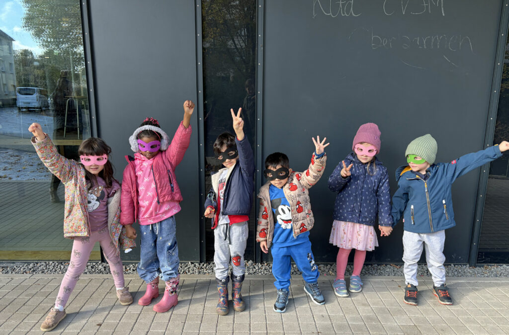 Kinder tragen Augenmasken und machen eine Siegerpose draussen vor der Kita