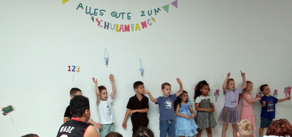 Die Vorschulkinder tanzen und singen unter dem bunten Schriftzug Alles Gute zum Schulanfang