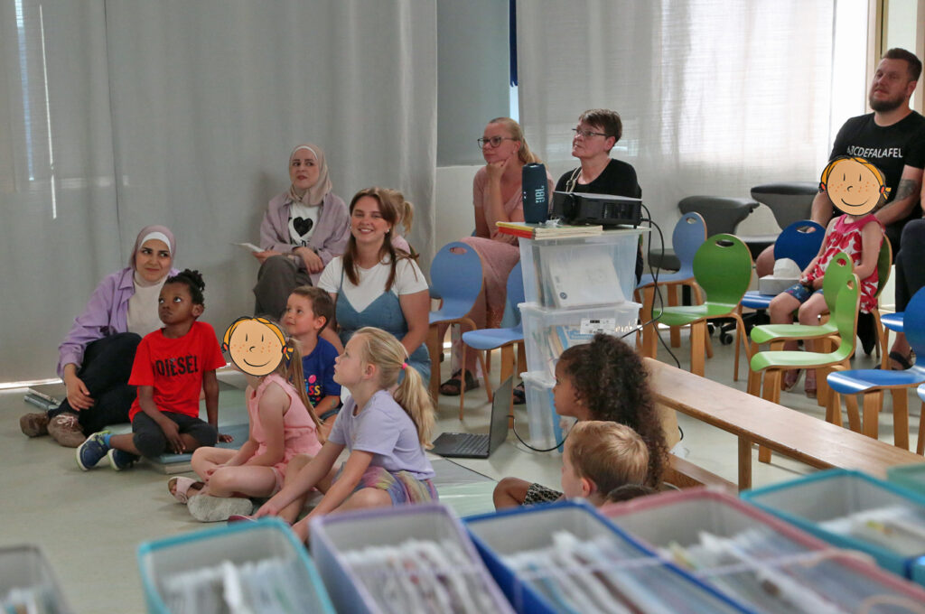 Kinder und Erwchsene hocken auf dem Fussboden und schauen zur Wand