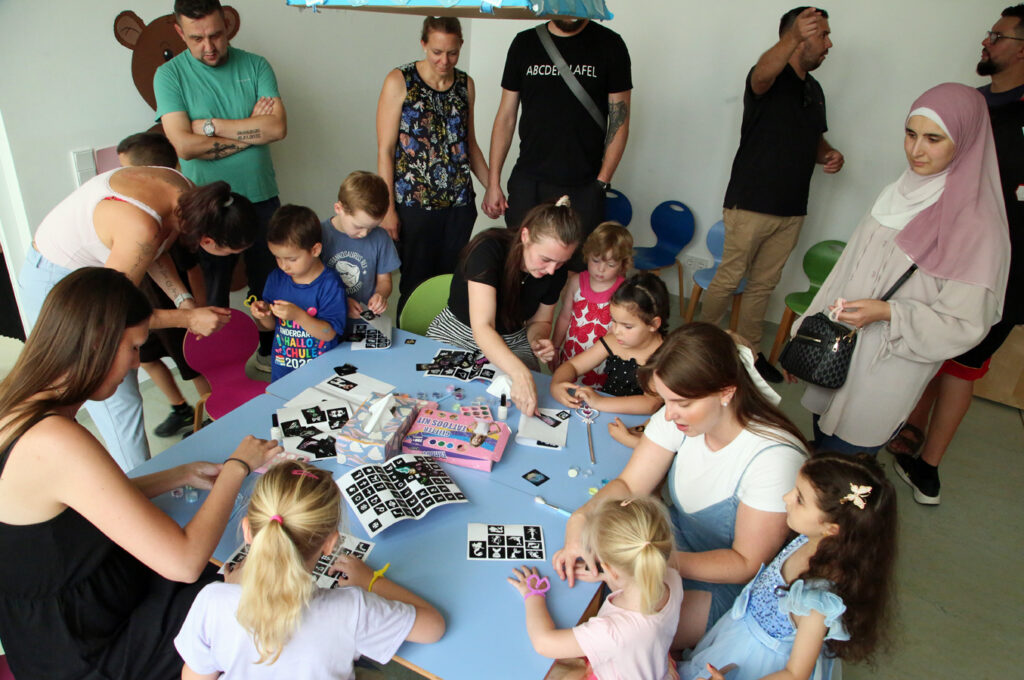 Kinder und Erwachsene sitzen am Tisch und die Kinder bekommen Glitzertattoos