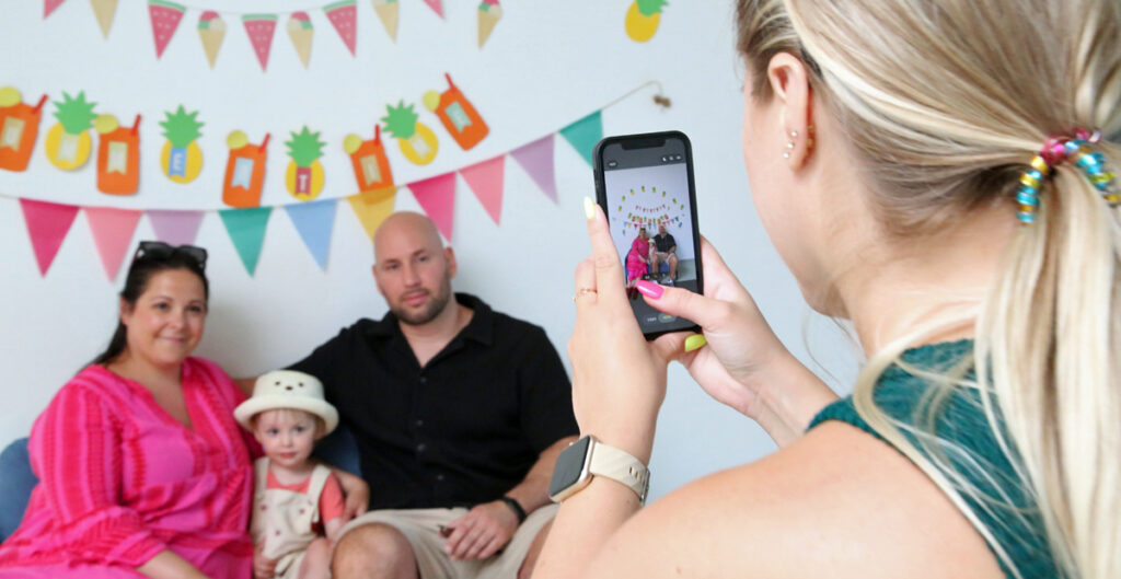 Eltern sitzen mit ihrem Kind unter bunten Wimpeln und werden fotografiiert