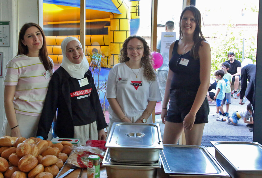 Vier Frauen stehen an einer Buffettheke und bereiten Hot-Dogs zu
