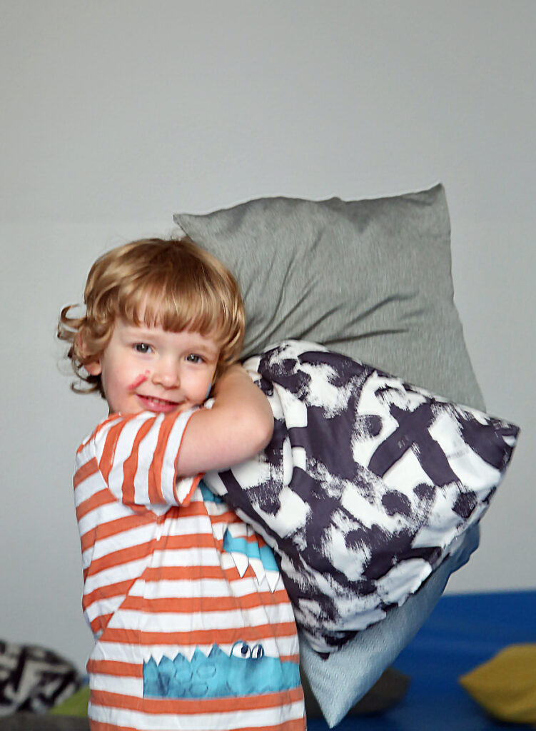 Ein Kind haelt mehrere bunte Kissen im Arm