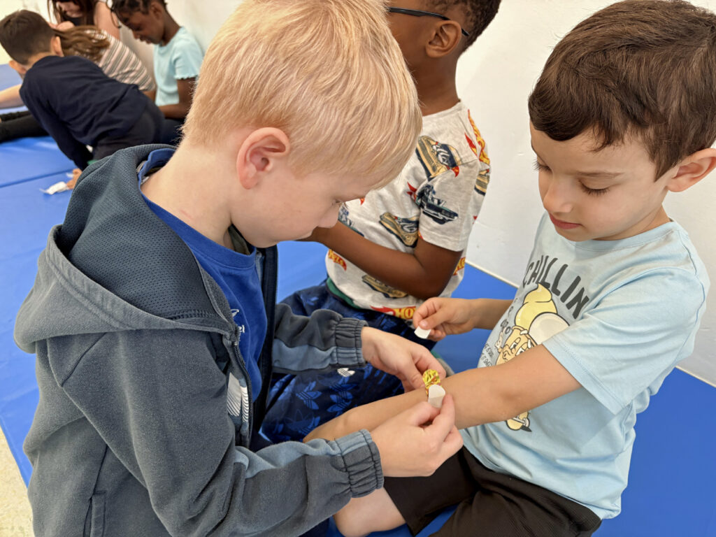 Ein Kind klebt einem anderen Kind ein buntes Pflaster auf den Arm