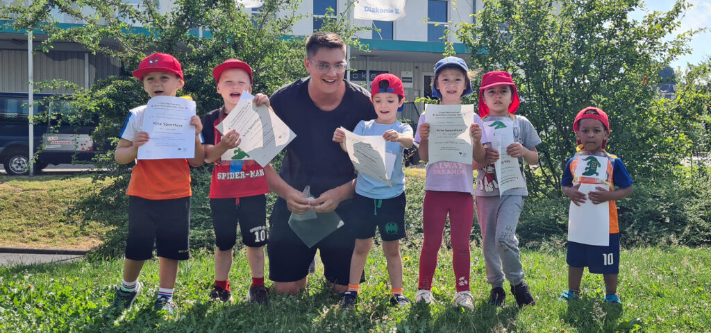 Kinder stehen neben einem Erzieher und zeigen ihre Urkunden über die Teilnahme am Kita-Sportfest