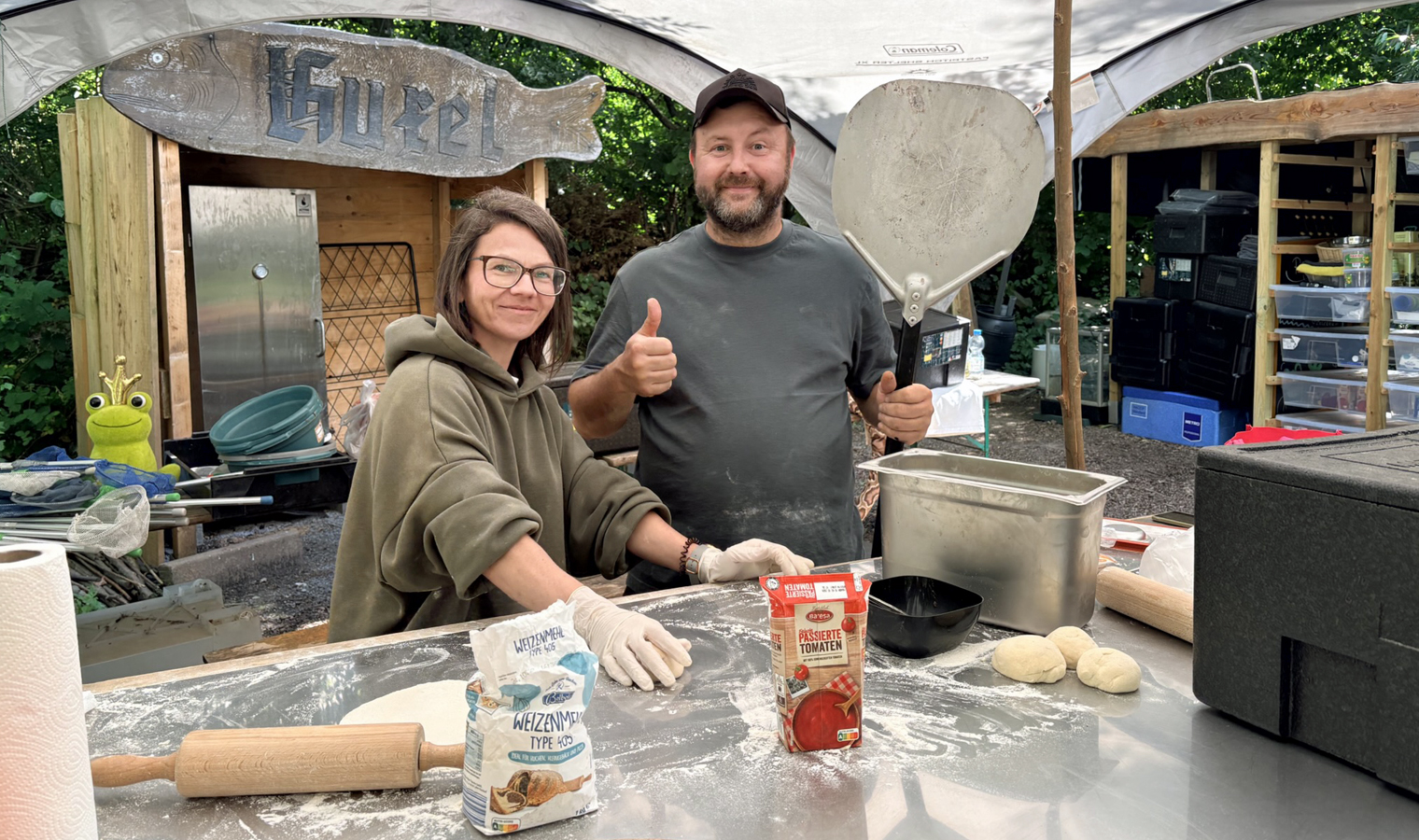 zwei Personen backen in einer Outdoor-Kueche Pizza