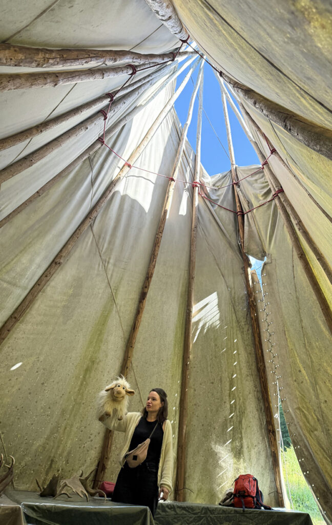 Eine Erzieherin steht in einem grossen Tipi und haelt eine Schaf-Handpuppe hoch