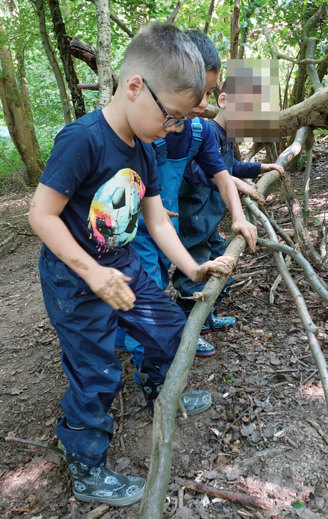 Kinder streichen Lehm auf einen waagerecht liegenden schmalen Baumstamm im Wald