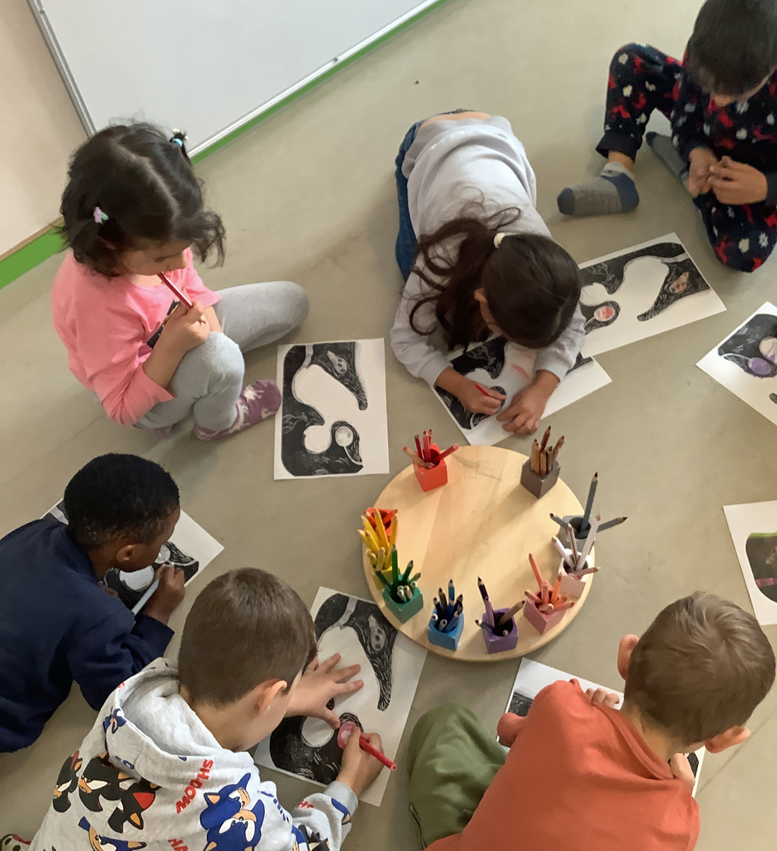 Kinder hocken auf dem Fussboden und malen mit Buntstiften