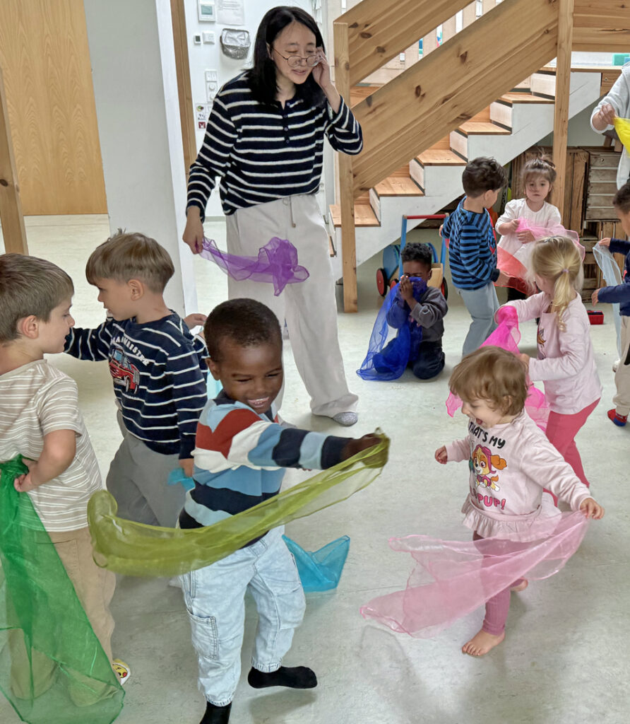 Kinder tanzen durch den Kita-Raum und schwingen bunte Tuecher